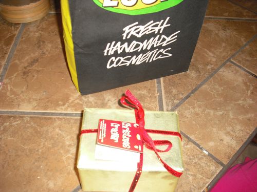 The Lush Giveaway Gift Shown Wrapped In Gold. Contains (1) Holiday Bath Bar & (1) Cinders Bath Bomb